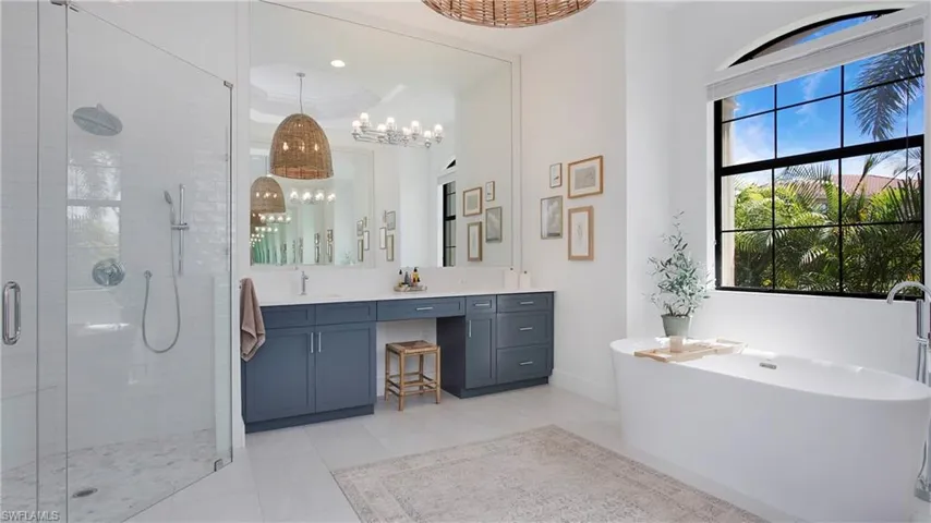 Bathroom featuring a stall shower, vanity, a chandelier, a freestanding tub, and baseboards