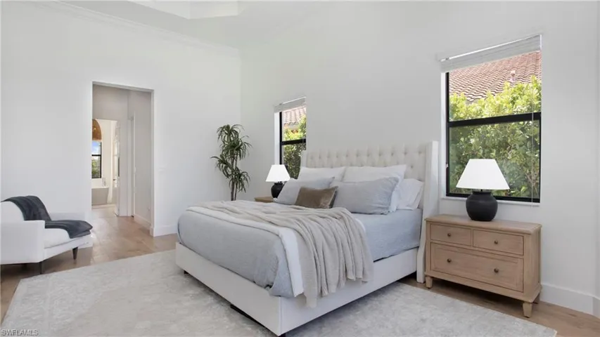 Bedroom with wood finished floors, crown molding, baseboards, and ensuite bath