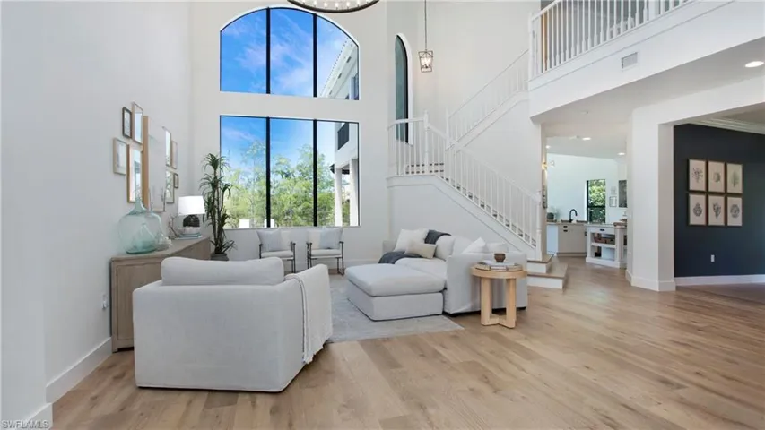 Living room featuring stairs, a high ceiling, light wood-type flooring, and baseboards