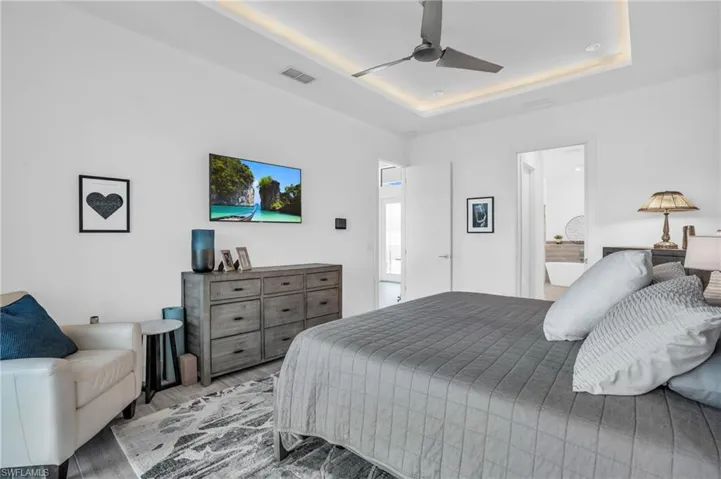 Bedroom featuring ceiling fan, a tray ceiling, connected bathroom, and wood-type flooring
