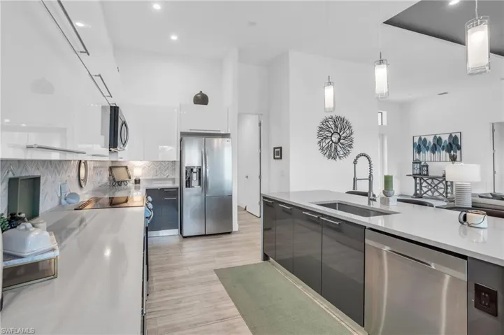 Kitchen with light hardwood / wood-style floors, hanging light fixtures, white cabinetry, appliances with stainless steel finishes, and sink