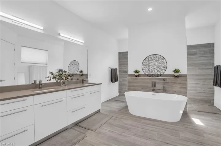 Bathroom with tile walls, tile flooring, a washtub, and dual bowl vanity