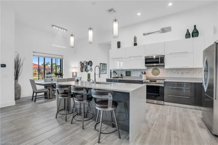Kitchen featuring light hardwood / wood-style flooring, backsplash, hanging light fixtures, white cabinetry, and appliances with stainless steel finishes