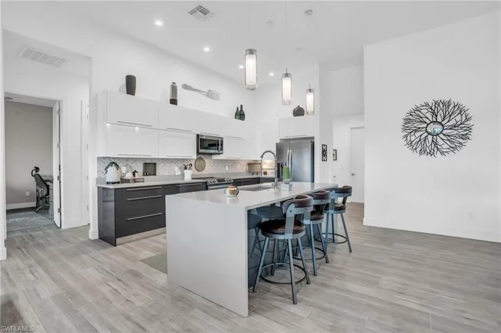 Kitchen with stainless steel appliances, backsplash, hanging light fixtures, a kitchen island with sink, and white cabinets