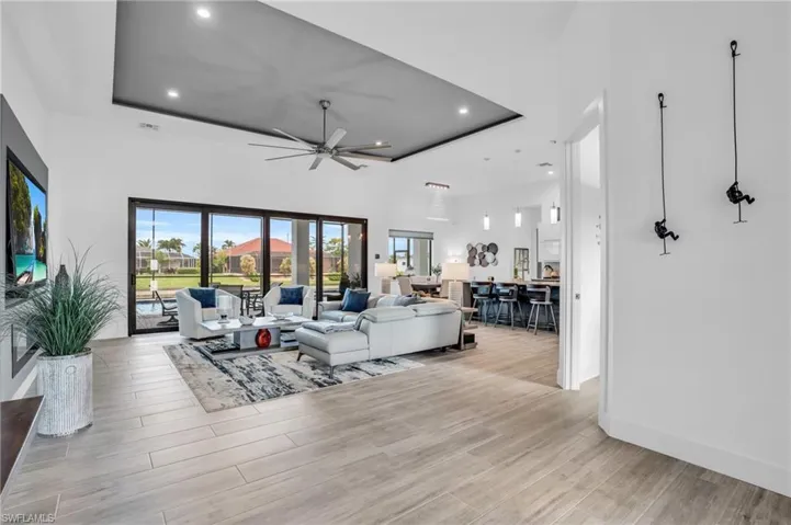 Living room with a raised ceiling, ceiling fan, a towering ceiling, and light wood-type flooring