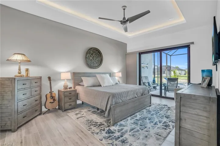 Bedroom featuring a tray ceiling, light hardwood / wood-style floors, access to outside, and ceiling fan