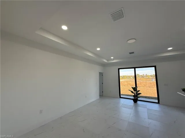 Recessed lighting illuminates a tray ceiling and white walls