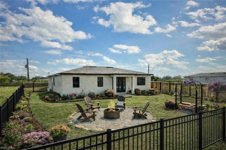 Fenced backyard featuring a gravel patio with a built-in fire pit, manicured lawn, and landscaped garden beds