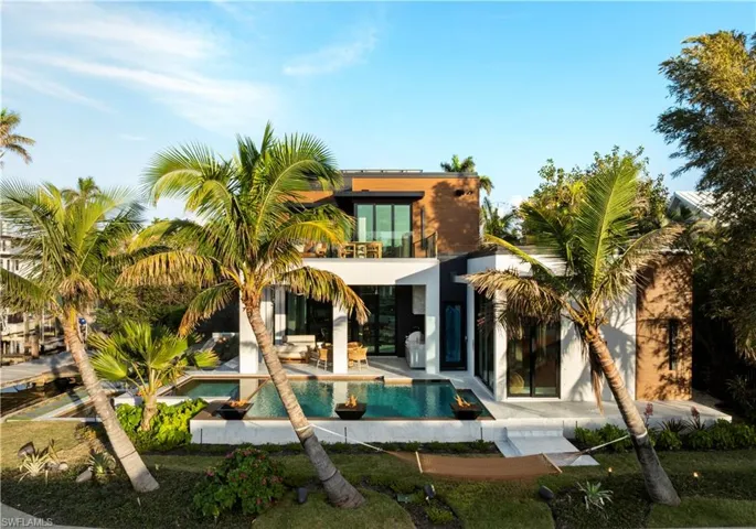 Rear view of property with a swimming pool with hot tub, a balcony, and a patio