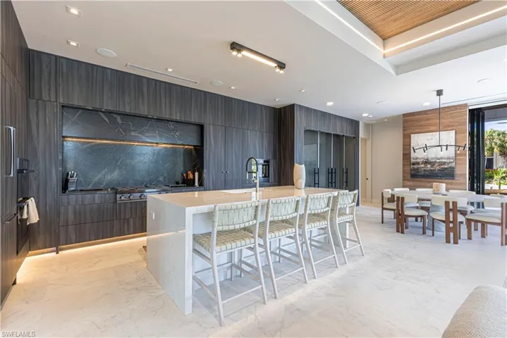 Kitchen featuring a marble waterfall island, a built in box effect marble hood area, and cabinets streching across the entire room encasing the custom temperature controlled wine room mirroring the water in the bay