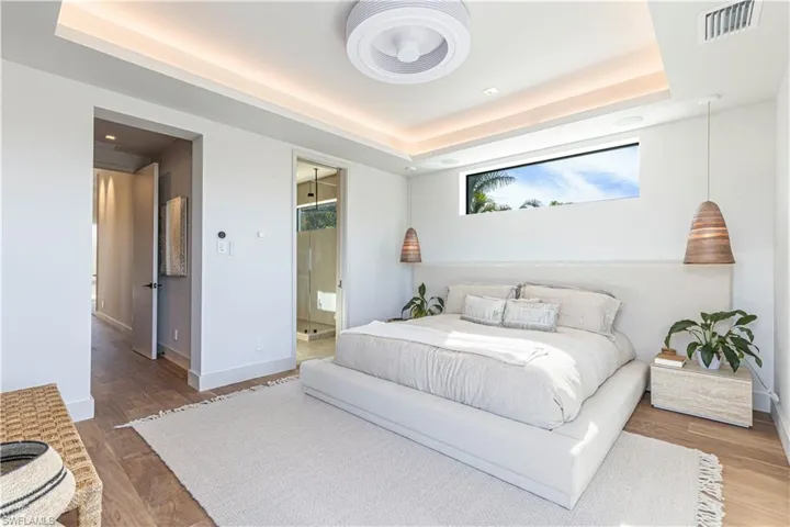 Upstairs master Bedroom featuring multiple windows, a tray ceiling, ensuite bath, and walnut floors
