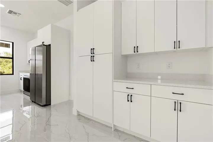 Kitchen with freestanding refrigerator, marble finish floor, and visible vents
