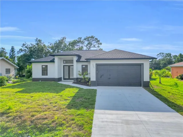 View of front of house with an attached garage, a front lawn, concrete driveway, french doors, and stucco siding