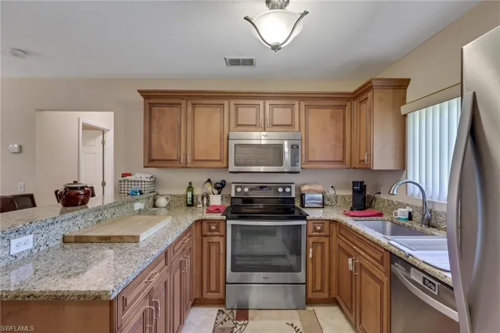 Kitchen with wood finish cabinetry, stainless steel appliances, a peninsula, and light stone counters