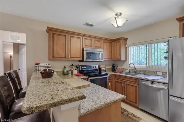 Kitchen with wood finish cabinetry, stainless steel appliances, a peninsula, and light stone counters