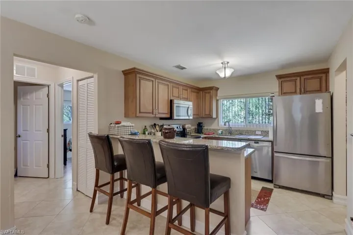 Kitchen featuring stainless steel appliances, a breakfast bar area, wood finish cabinetry, light stone countertops, and a peninsula