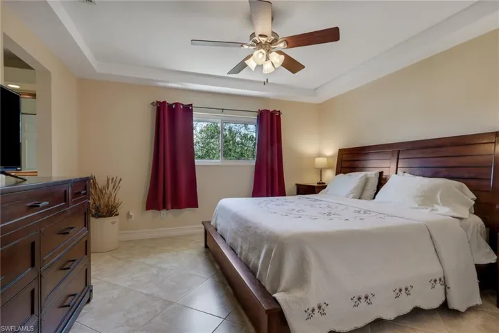 Bedroom featuring ceiling fan, a raised ceiling, and light tile patterned floors