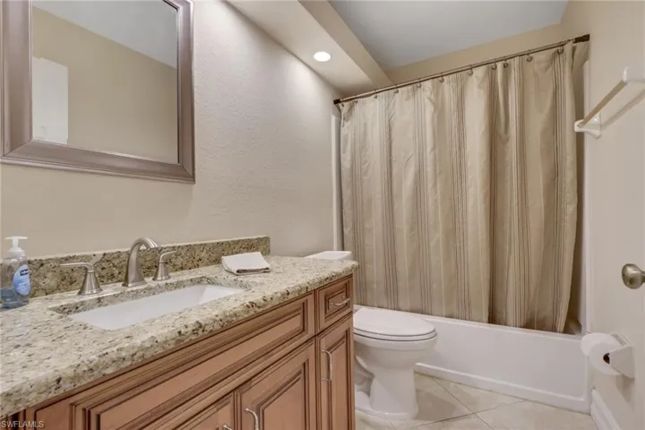 Full bathroom featuring vanity, a textured wall, shower / bath combination with curtain, light tile patterned flooring, and recessed lighting