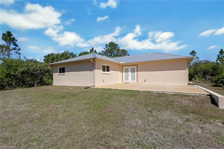 Rear view of property featuring a lawn, stucco siding, a patio area, and french doors