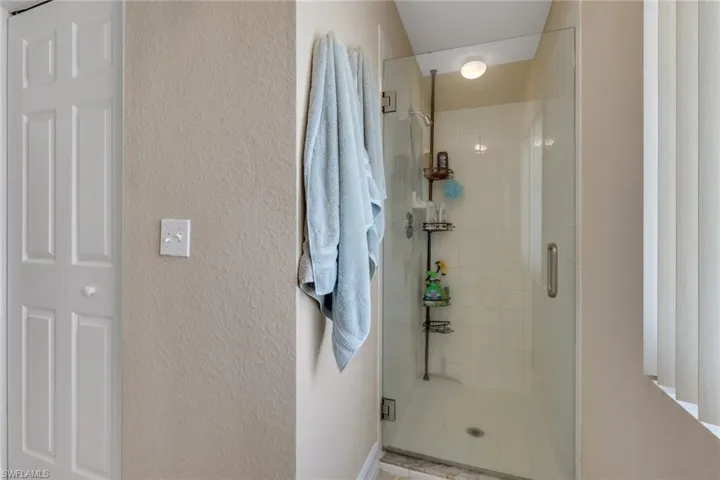 Bathroom with a shower stall, a textured wall, and a closet