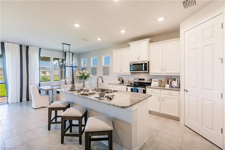 Kitchen featuring white cabinetry, sink, light stone countertops, a center island with sink, and appliances with stainless steel finishes