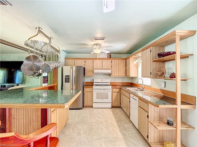 Kitchen with white appliances, light tile patterned floors, kitchen peninsula, light brown cabinetry, and sink