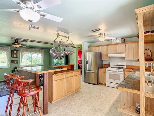 Kitchen featuring stainless steel fridge, sink, light tile patterned floors, white gas stove, and ceiling fan