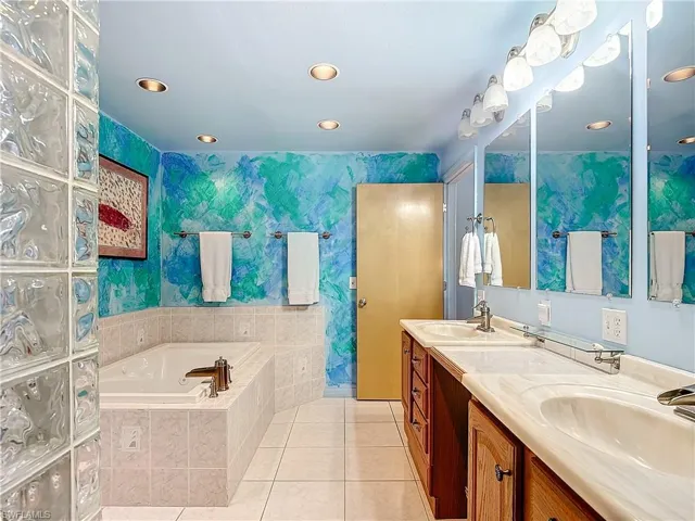 Bathroom with double sink vanity, tile patterned flooring, and a relaxing tiled tub