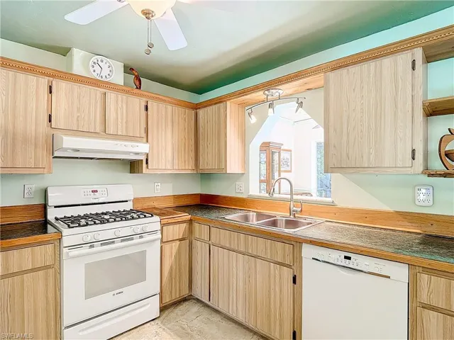 Kitchen with white appliances, light brown cabinets, sink, light tile patterned floors, and ceiling fan