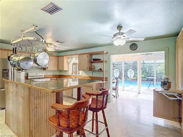 Kitchen with light tile patterned flooring, ceiling fan, white range with gas stovetop, a kitchen bar, and tile countertops