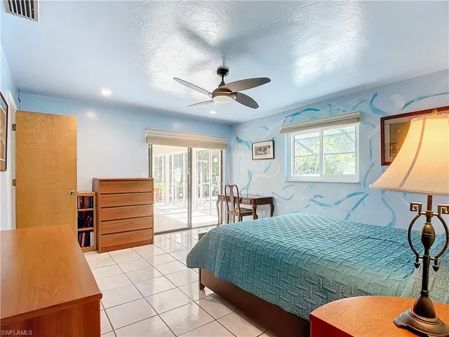Tiled bedroom featuring multiple windows, access to exterior, and ceiling fan