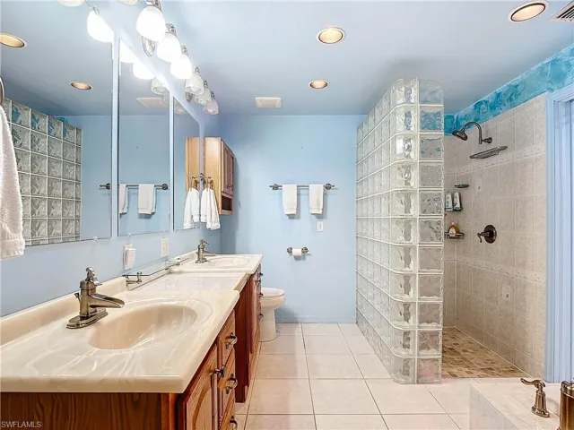 Bathroom featuring dual vanity, toilet, a tile shower, and tile patterned flooring