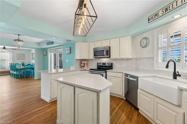 Kitchen with stainless steel appliances, wood-type flooring, a center island, and decorative light fixtures