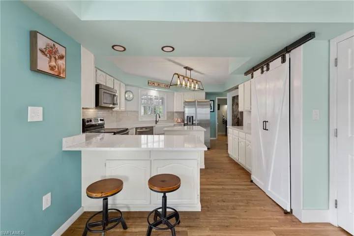 Kitchen featuring kitchen peninsula, stainless steel appliances, backsplash, light wood-type flooring, and white cabinets