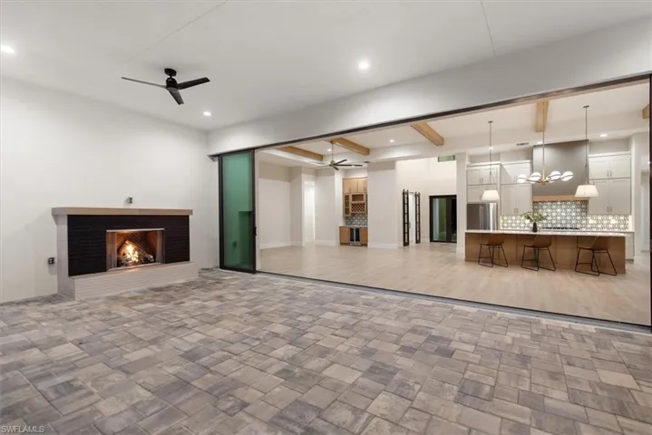 Unfurnished living room featuring beam ceiling, a ceiling fan, a chandelier, a brick fireplace, and recessed lighting