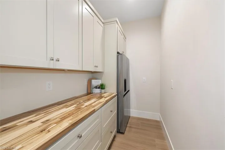 Kitchen featuring white cabinetry, stainless steel fridge, light wood-type flooring, and wood counters