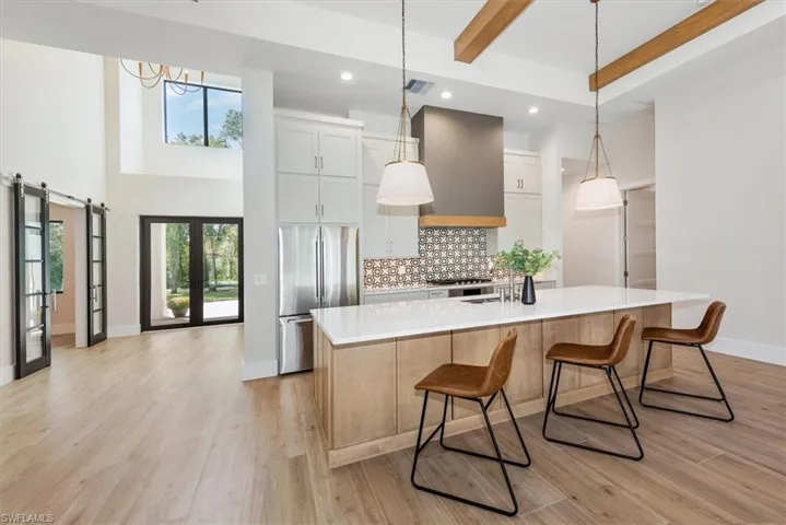 Kitchen with decorative backsplash, plenty of natural light, stainless steel fridge, white cabinets, and beam ceiling