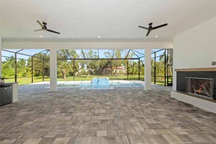 View of patio featuring ceiling fan, a sunroom, a lit fireplace, and a lanai