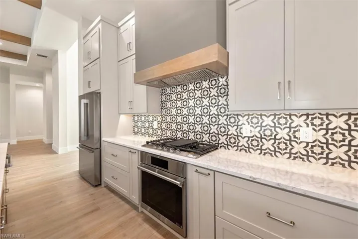 Kitchen featuring appliances with stainless steel finishes, custom range hood, tasteful backsplash, light stone countertops, and light wood finished floors
