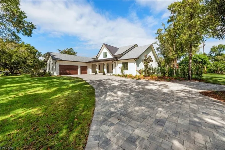 Modern inspired farmhouse with a front yard, covered porch, an attached garage, and decorative driveway