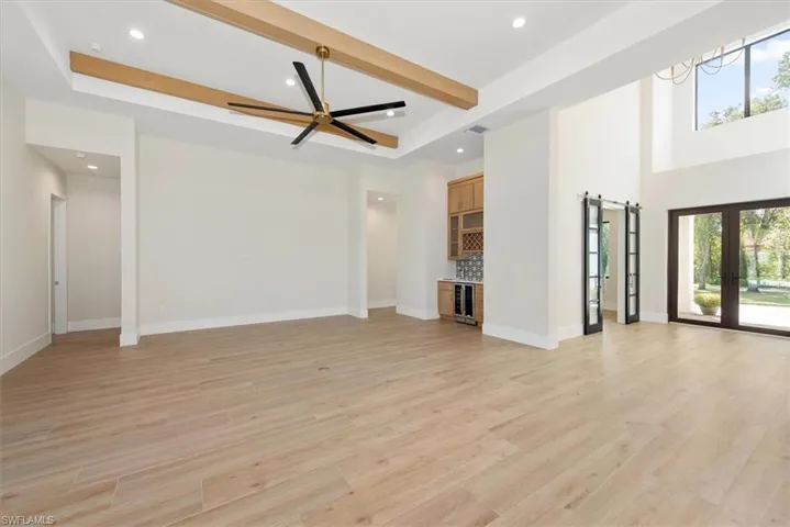 Unfurnished living room featuring a barn door, light wood finished floors, bar area, wine cooler, and beamed ceiling