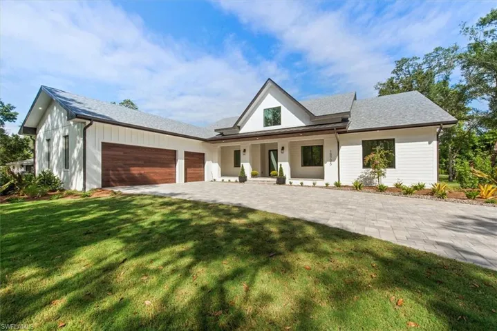 Modern inspired farmhouse featuring covered porch, an attached garage, a front lawn, and decorative driveway