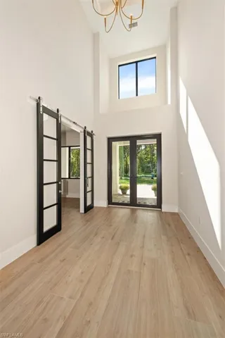 Entrance foyer with a barn door, french doors, light wood finished floors, a high ceiling, and a chandelier