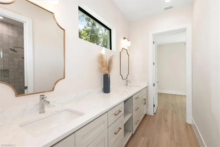Full bathroom with tiled shower, double vanity, and light wood-style floors