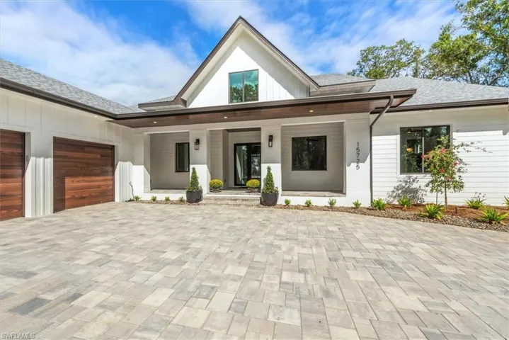 Modern inspired farmhouse featuring covered porch, roof with shingles, decorative driveway, and an attached garage