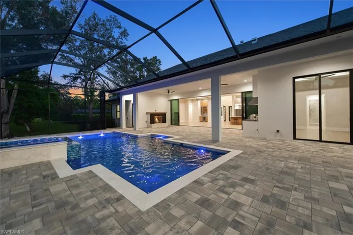 Pool at dusk featuring an outdoor pool, a patio area, glass enclosure, and a sunroom