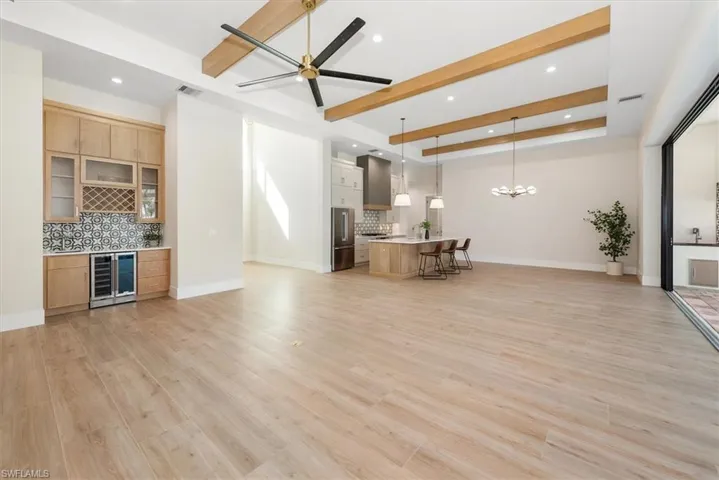 Living area featuring beam ceiling, light wood-style floors, beverage cooler, a dry bar, and recessed lighting