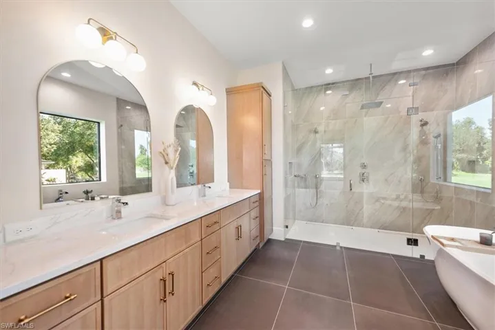 Full bath with plenty of natural light, double vanity, a freestanding bath, dark tile patterned flooring, and recessed lighting