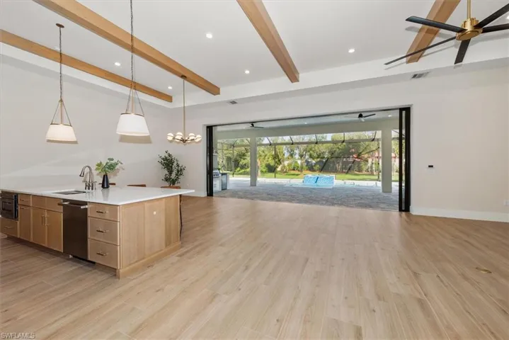 Kitchen with hanging light fixtures, open floor plan, beam ceiling, a sunroom, and light stone countertops
