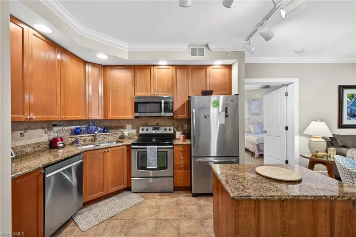 Kitchen with ornamental molding, dark stone countertops, stainless steel appliances, wood finish cabinetry, and tasteful backsplash